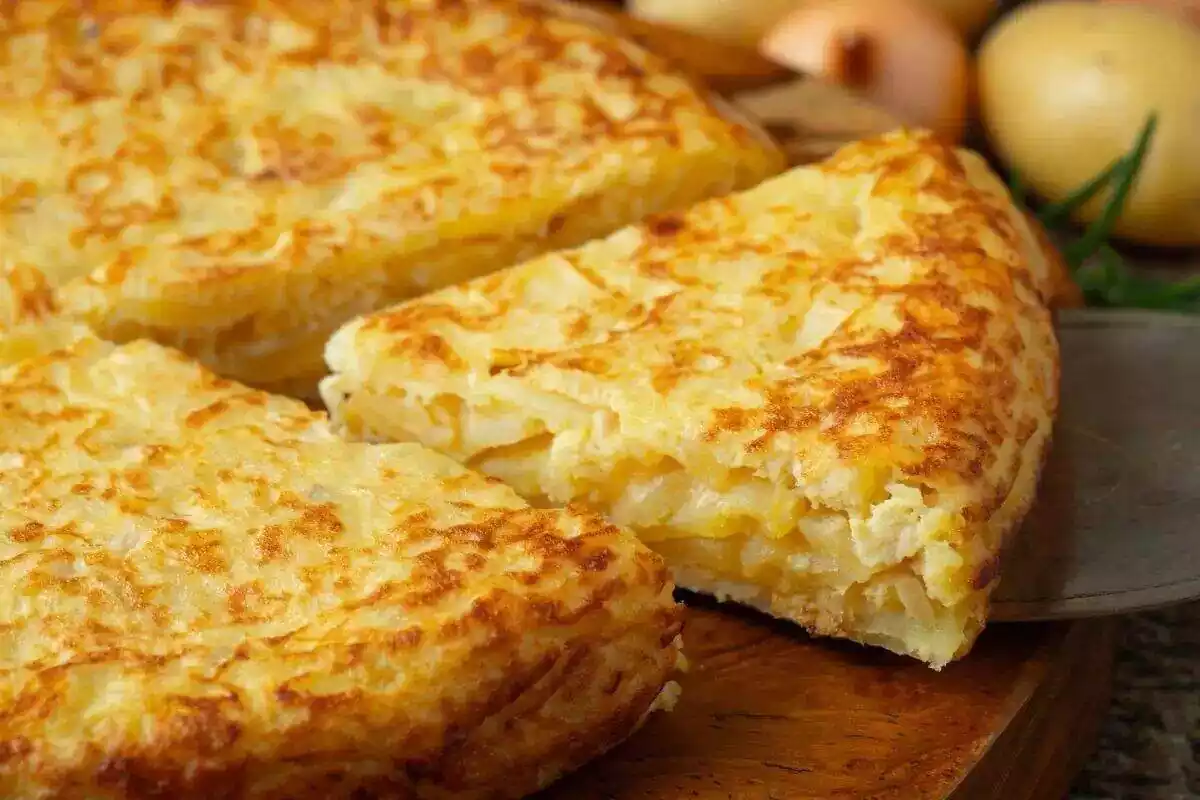 Foto de una tortilla de patata sobre una madera de la que se ve una parte y un triángulo cortado