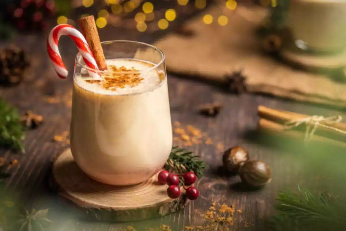 Foto de un vaso de ponche navideño con un bastón y canela dentro colocado sobre una base de madera redonda y de fondo decoración navideña desenfocada Foto de un vaso de ponche navideño con un bastón y canela dentro colocado sobre una base de madera redonda y de fondo decoración navideña desenfocada