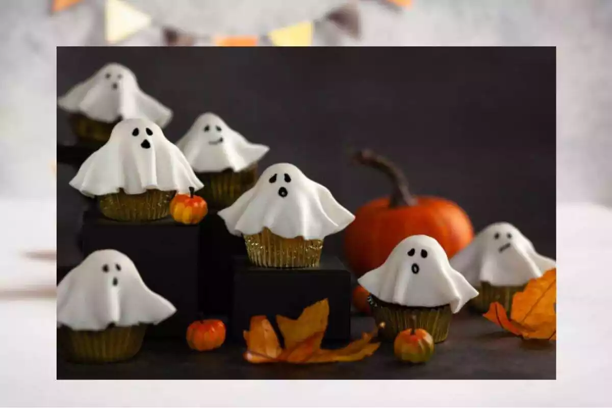 Foto de siete magdalenas con fondant blanco por encima con una cara pintada para que sean fantasmas con una hoja de otoño y una calabaza decorativa desenfocada de fondo. Detrás una foto desenfocada Foto de siete magdalenas con fondant blanco por encima con una cara pintada para que sean fantasmas con una hoja de otoño y una calabaza decorativa desenfocada de fondo. Detrás una foto desenfocada